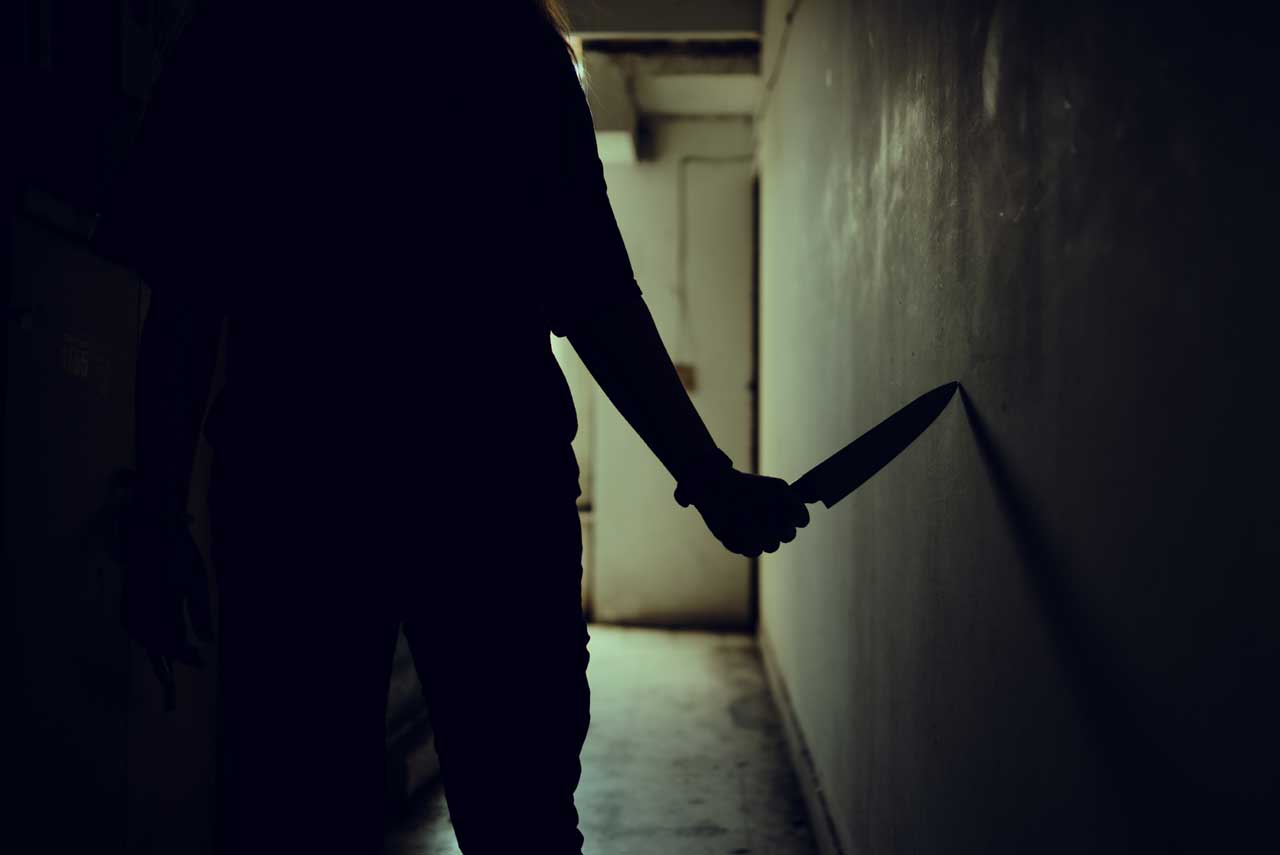 Person geht mit Messer in der Hand durch dunklen Flur.